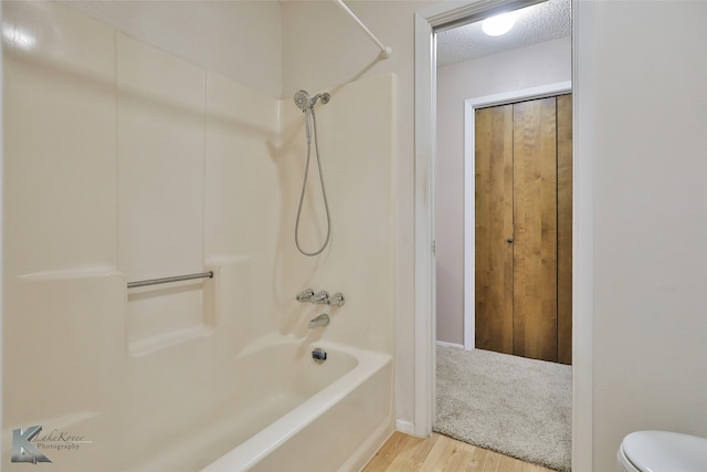 bathroom with shower / washtub combination, a textured ceiling, hardwood / wood-style flooring, and toilet