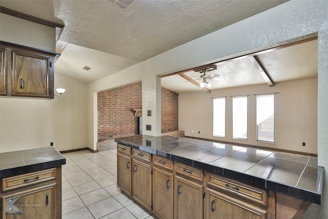 kitchen with tile countertops, a textured ceiling, vaulted ceiling, and ceiling fan