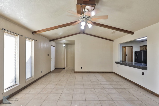 tiled spare room featuring a textured ceiling, lofted ceiling with beams, ceiling fan, and a wealth of natural light