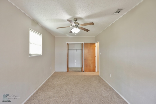 unfurnished bedroom featuring light carpet, a textured ceiling, a closet, and ceiling fan