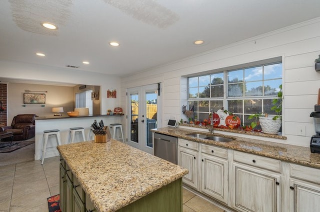 kitchen featuring stainless steel dishwasher, sink, light stone counters, and a center island