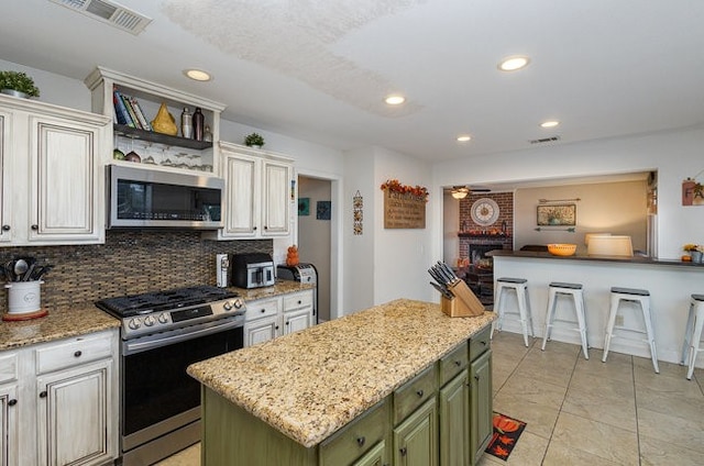 kitchen with green cabinets, appliances with stainless steel finishes, light stone countertops, a fireplace, and a kitchen island