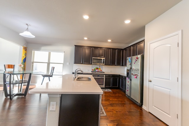 kitchen featuring appliances with stainless steel finishes, a kitchen island with sink, dark hardwood / wood-style floors, pendant lighting, and sink