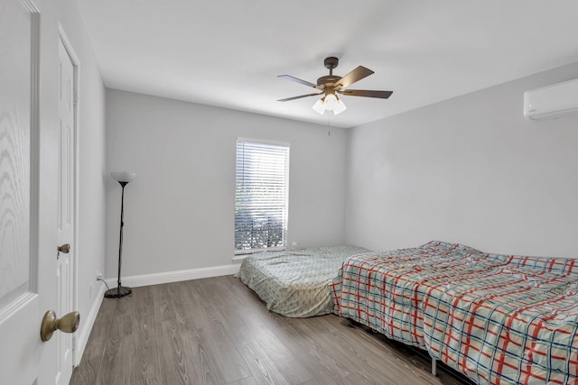 bedroom featuring a wall mounted air conditioner, wood-type flooring, and ceiling fan