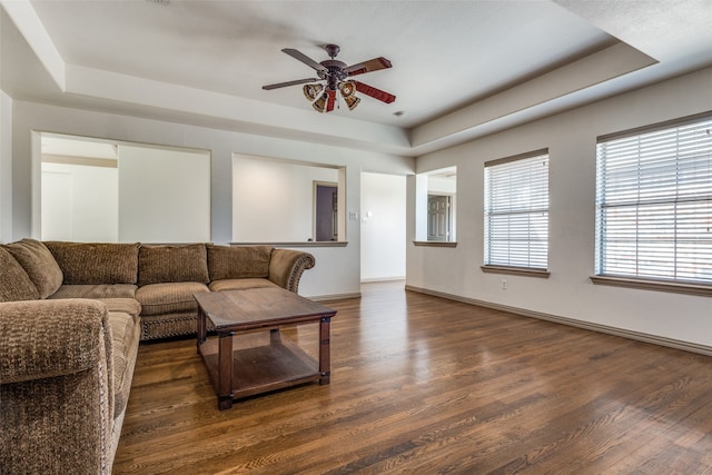 living room with ceiling fan, a tray ceiling, and dark hardwood / wood-style floors