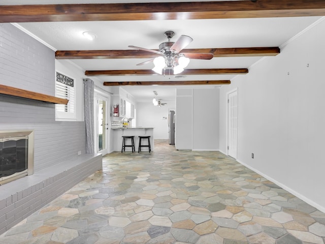 unfurnished living room featuring beamed ceiling, ornamental molding, brick wall, and ceiling fan