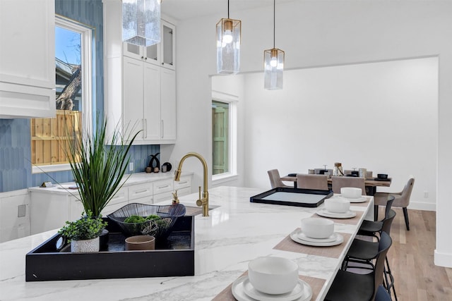 kitchen featuring light stone counters, backsplash, decorative light fixtures, white cabinets, and light wood-type flooring