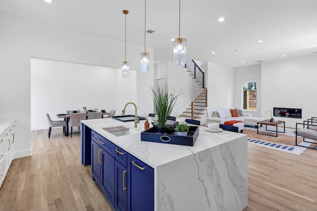 kitchen featuring pendant lighting, blue cabinets, sink, light wood-type flooring, and light stone counters