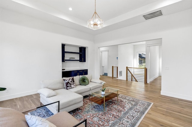 living room featuring a notable chandelier, a raised ceiling, and light wood-type flooring