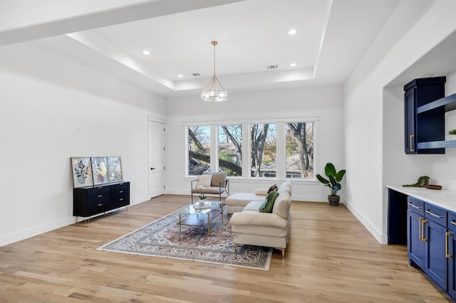 living room featuring light hardwood / wood-style floors, a raised ceiling, and a chandelier