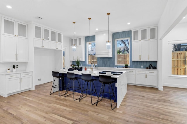 kitchen with a kitchen breakfast bar, light hardwood / wood-style flooring, an island with sink, decorative light fixtures, and white cabinets