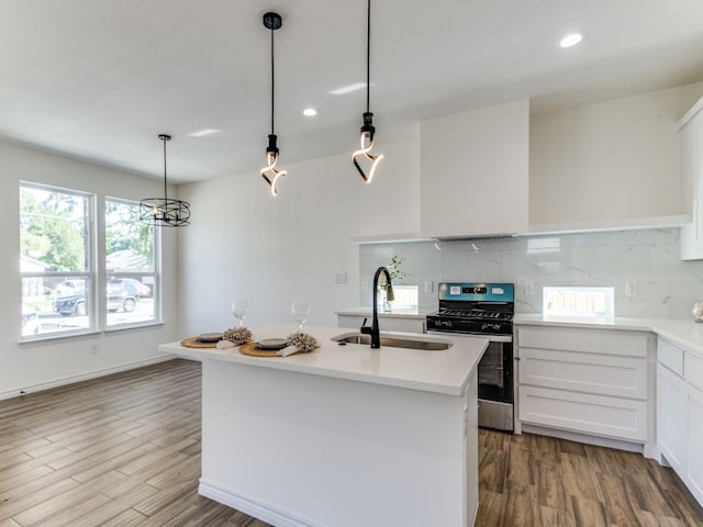 kitchen with a kitchen island with sink, stainless steel gas stove, hardwood / wood-style floors, sink, and white cabinets