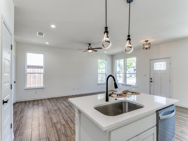 kitchen featuring light wood-type flooring, hanging light fixtures, white cabinetry, stainless steel dishwasher, and a kitchen island with sink