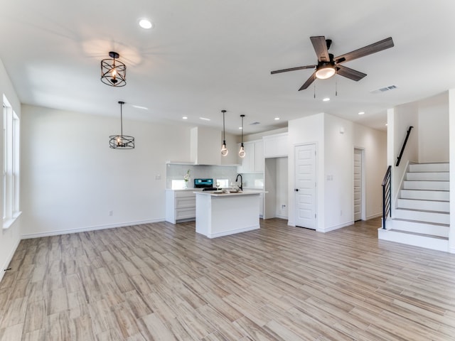 kitchen with white cabinetry, light hardwood / wood-style flooring, decorative light fixtures, and a kitchen island with sink