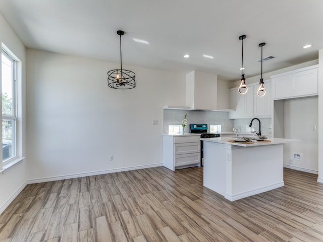 kitchen featuring light hardwood / wood-style flooring, white cabinetry, a center island with sink, and range