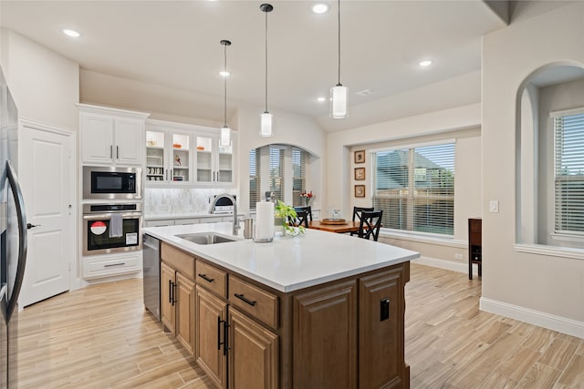 kitchen with appliances with stainless steel finishes, light wood-type flooring, sink, white cabinets, and an island with sink