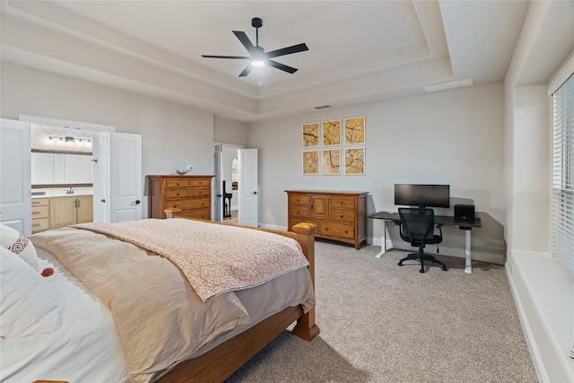 carpeted bedroom featuring a raised ceiling, ensuite bathroom, sink, and ceiling fan