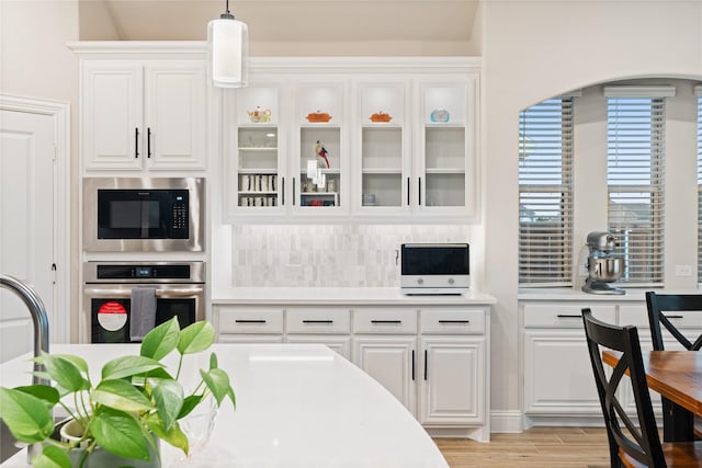 kitchen with tasteful backsplash, stainless steel appliances, pendant lighting, light hardwood / wood-style flooring, and white cabinets