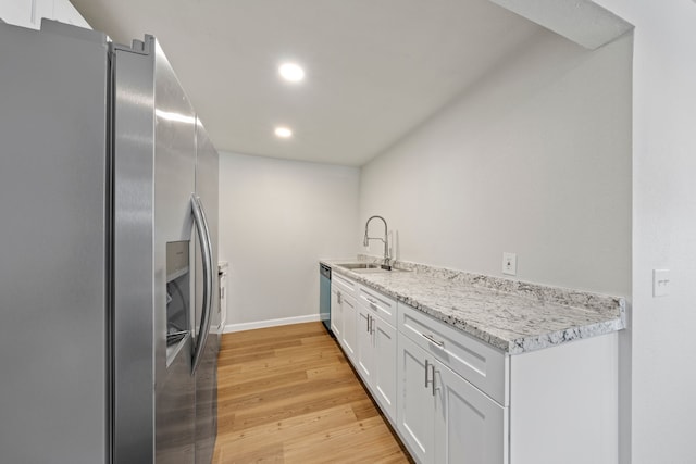 kitchen with appliances with stainless steel finishes, white cabinetry, sink, light stone counters, and light hardwood / wood-style flooring