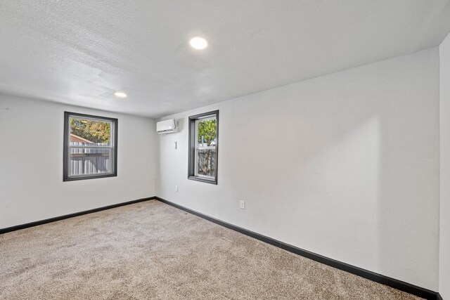 carpeted empty room with a wealth of natural light, a textured ceiling, and a wall unit AC