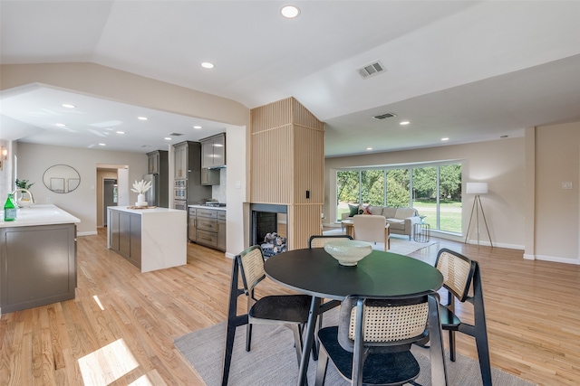 dining area with a large fireplace, sink, vaulted ceiling, and light hardwood / wood-style floors