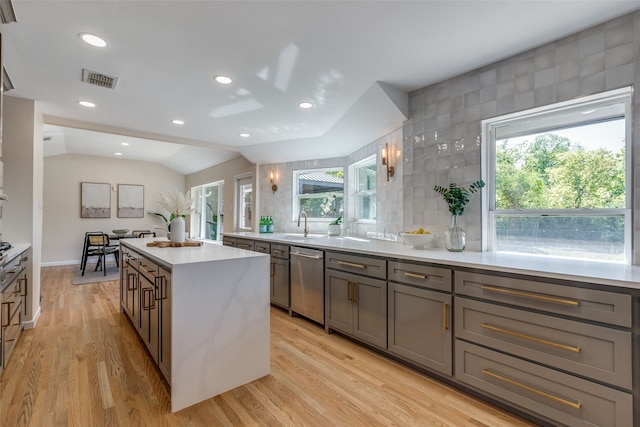 kitchen with lofted ceiling, backsplash, a kitchen island, stainless steel dishwasher, and light hardwood / wood-style flooring