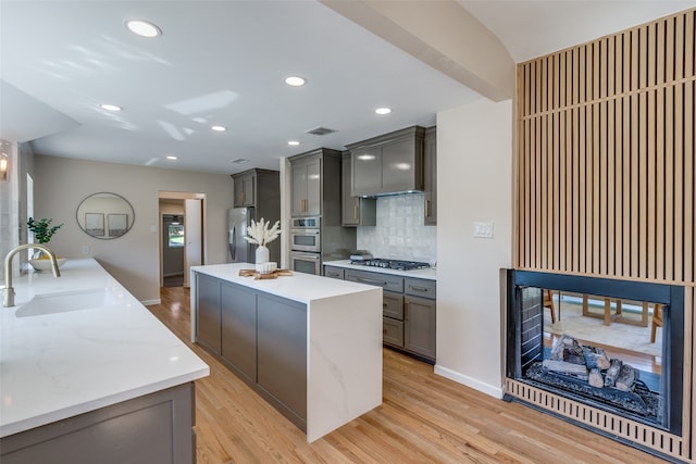 kitchen with decorative backsplash, light wood-type flooring, stainless steel appliances, sink, and a center island