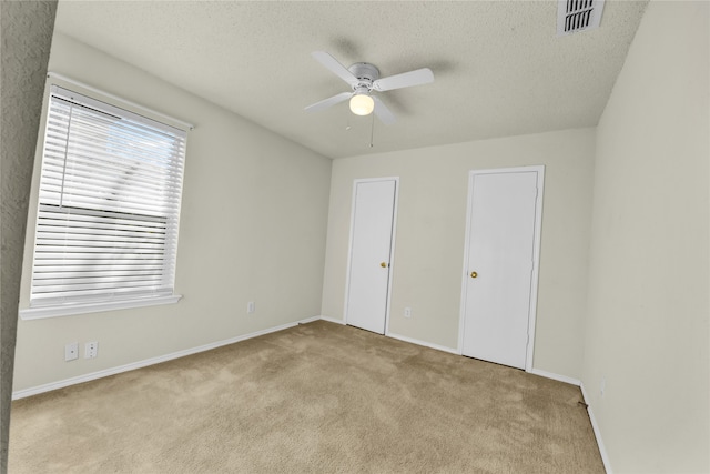 unfurnished bedroom featuring light carpet, a textured ceiling, and ceiling fan