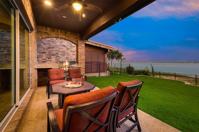 patio terrace at dusk with an outdoor fire pit, a ceiling fan, area for grilling, a water view, and a yard