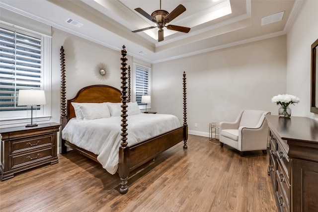 bedroom featuring ceiling fan, a tray ceiling, ornamental molding, and wood-type flooring