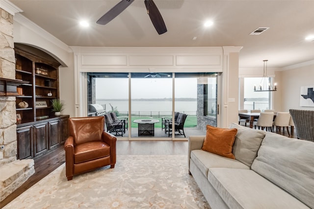 living room with ornamental molding, a water view, wood-type flooring, and ceiling fan with notable chandelier