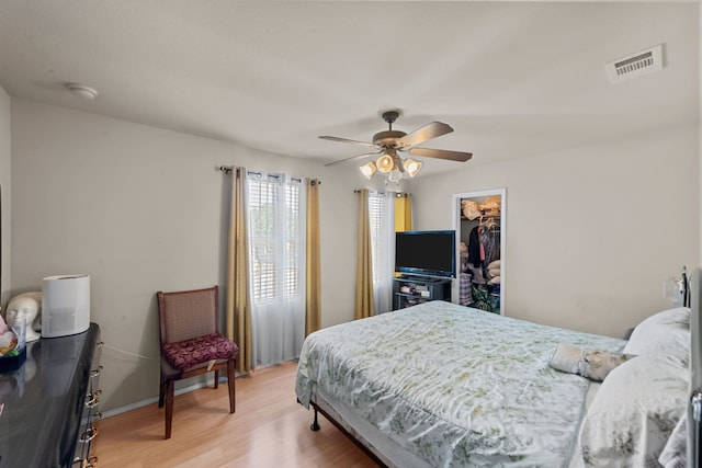 bedroom featuring a walk in closet, wood-type flooring, a closet, and ceiling fan