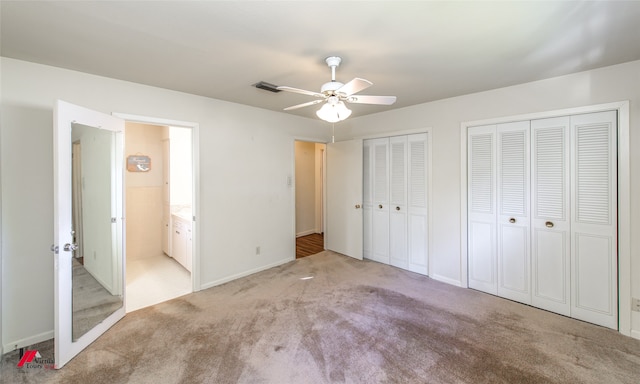 unfurnished bedroom featuring ensuite bathroom, two closets, light colored carpet, and ceiling fan