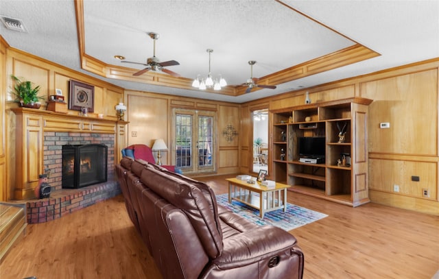 living room with a brick fireplace, a tray ceiling, and light wood-type flooring