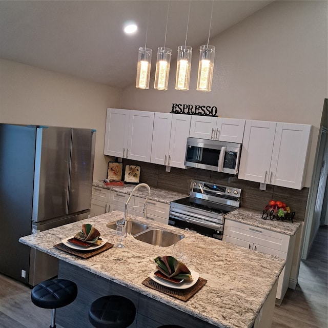 kitchen with sink, hanging light fixtures, stainless steel appliances, white cabinets, and a kitchen island with sink