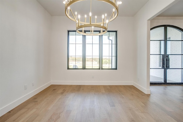 spare room featuring french doors, a chandelier, and light hardwood / wood-style floors