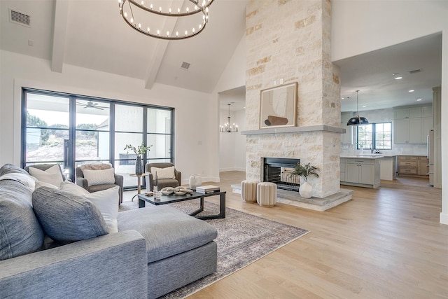 living room with sink, a stone fireplace, beamed ceiling, high vaulted ceiling, and light wood-type flooring