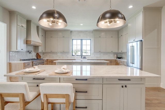 kitchen with light stone countertops, custom range hood, premium appliances, decorative light fixtures, and light hardwood / wood-style floors