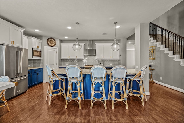 kitchen featuring wall chimney exhaust hood, a kitchen breakfast bar, hanging light fixtures, stainless steel appliances, and blue cabinets