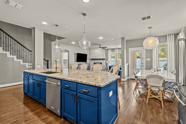 kitchen with an island with sink, sink, decorative light fixtures, blue cabinets, and dark hardwood / wood-style flooring