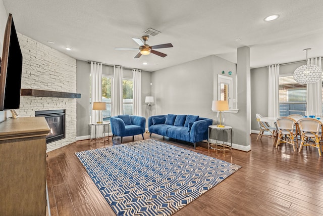 living room with a stone fireplace, dark hardwood / wood-style floors, a textured ceiling, and ceiling fan