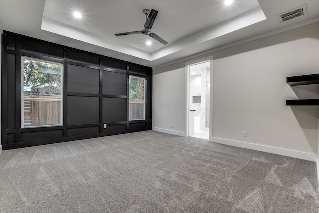 empty room featuring a healthy amount of sunlight, ceiling fan, a raised ceiling, and carpet floors