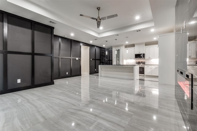 kitchen with hanging light fixtures, stainless steel appliances, a tray ceiling, a center island, and white cabinets