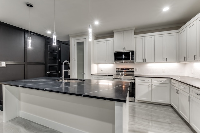 kitchen featuring appliances with stainless steel finishes, hanging light fixtures, a kitchen island with sink, and white cabinets