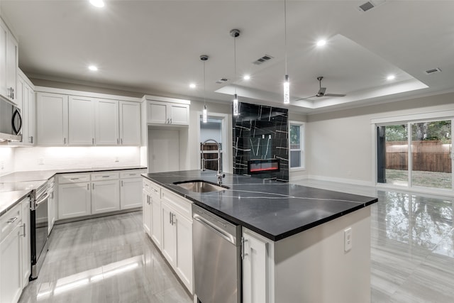 kitchen with an island with sink, hanging light fixtures, sink, white cabinets, and appliances with stainless steel finishes