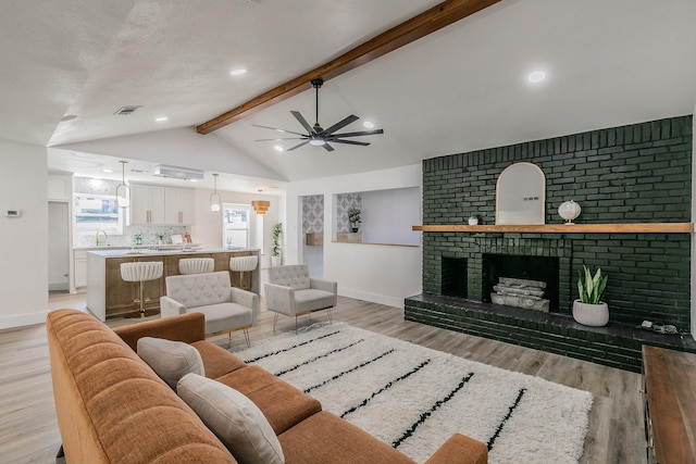 living room with sink, a fireplace, ceiling fan, light hardwood / wood-style flooring, and lofted ceiling with beams