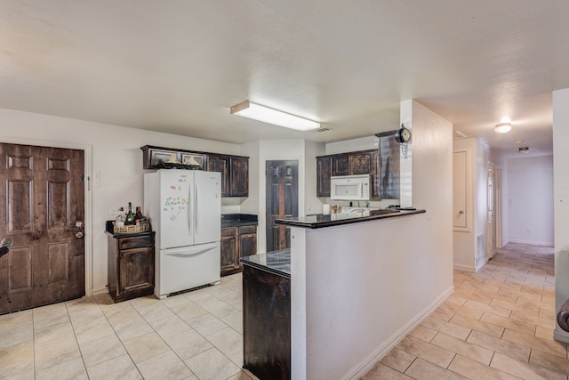 kitchen featuring dark brown cabinetry, a textured ceiling, white appliances, and kitchen peninsula