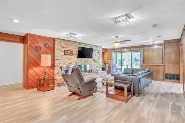 living room featuring ceiling fan, a textured ceiling, a brick fireplace, wood walls, and light hardwood / wood-style floors