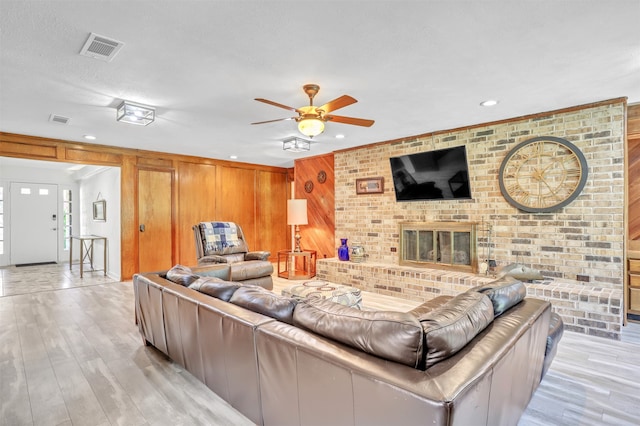 living room featuring wooden walls, brick wall, a brick fireplace, a textured ceiling, and light hardwood / wood-style floors