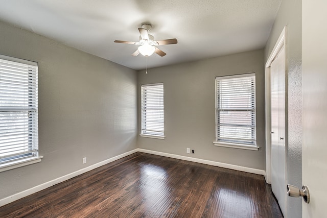 spare room featuring a healthy amount of sunlight, dark wood-type flooring, and ceiling fan